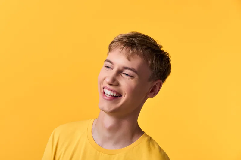 Smiling young man in a yellow studio backdrop, showcasing happiness and positive energy, casual tee, bright lighting, candid joy, lifestyle photography for cheerful branding