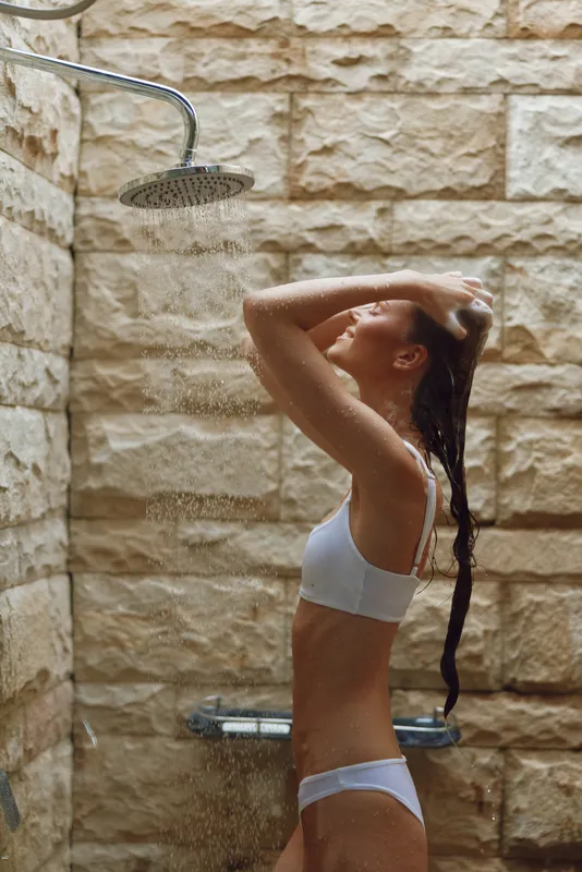 woman showering outdoors under rainfall with stone wall background, wearing white underwear, relaxing and cleansing, natural light, wellness concept