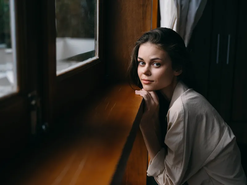 Портрет молодой женщины дома у окна с деревянной рамой