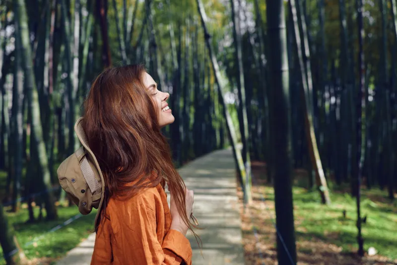 Woman redhead smile park path hat portrait of a happy young woman standing on a tree-lined forest path, eyes closed and smiling, casual outfit and straw hat on backpack.