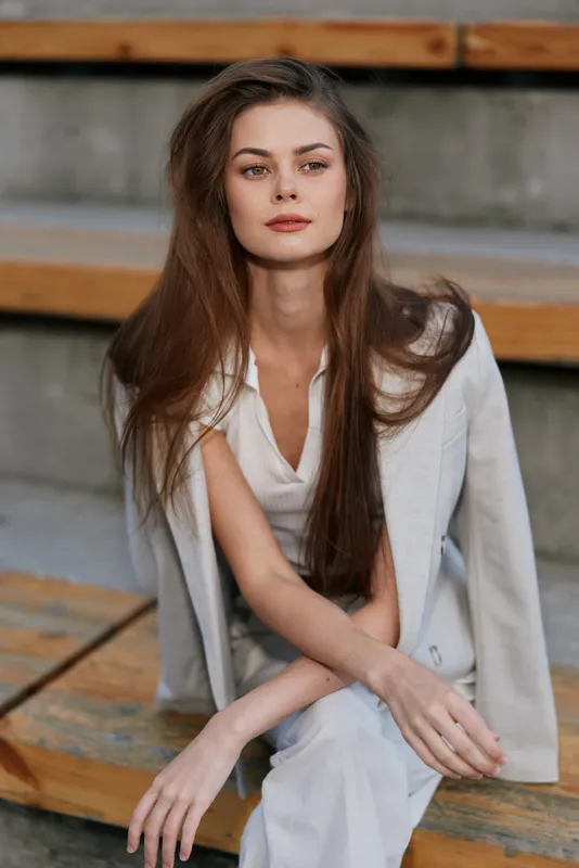 woman with long brown hair in white suit sitting on wooden stairs confident serious look fashion business style outdoor shot autumn color palette