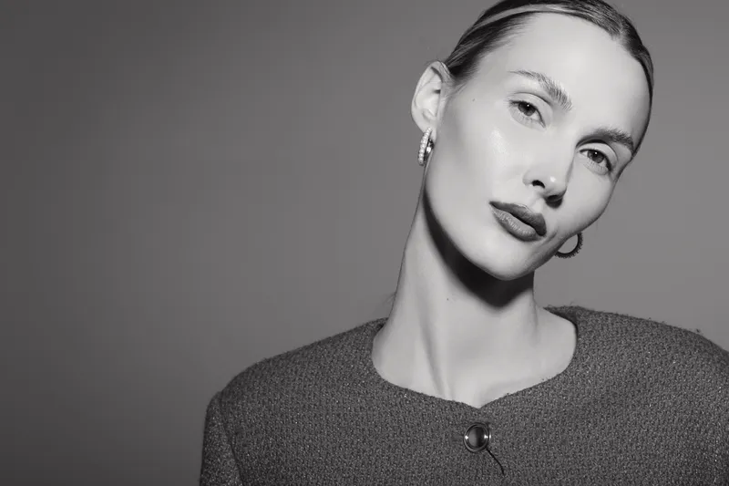 Portrait of a young white woman with pale skin and slicked back hair wearing a textured top with a button on a grey background. Concept for fashion and minimalistic beauty.
