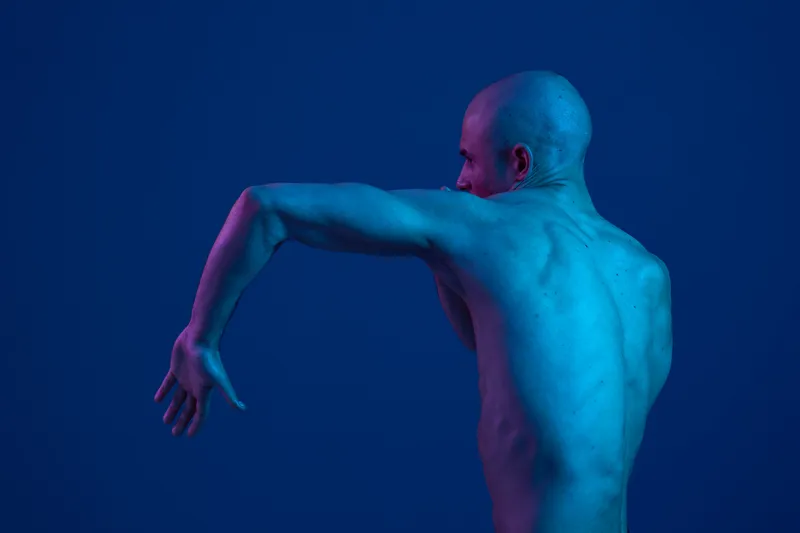Athletic man posing against a blue background, showcasing dynamic movement with vivid lighting. The image captures strength, energy, and artistry.