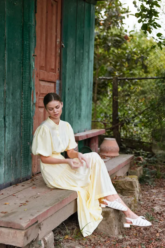 woman sitting outdoor dress yellow serene porch steps calm rustic, image shows a woman on a wooden porch outdoors gazing downward creating a peaceful calm mood in a garden setting