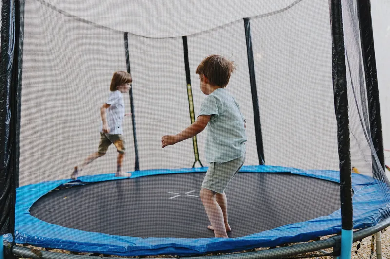 Two playful children having fun on a trampoline, enjoying outdoor activities with happiness and energy, surrounded by a vibrant atmosphere of summer.