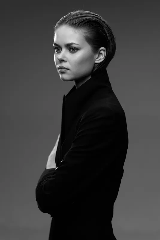 Black and white portrait of a serious woman with crossed arms wearing a dark jacket and slicked-back hair.