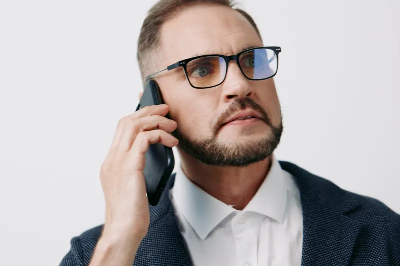 A focused business professional speaks on a mobile phone against an isolated colored background, conveying confidence, determination, and calm leadership in a corporate setting.