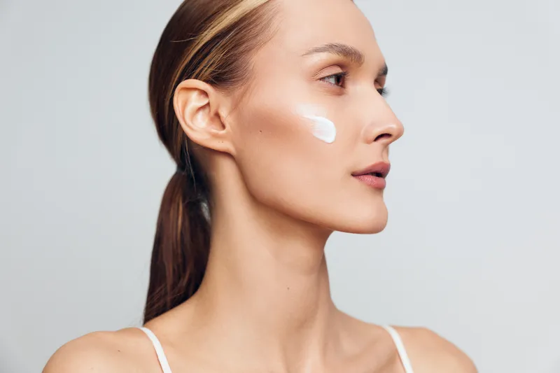 Woman applying face cream, skincare self care close up profile on a light gray background, soft studio lighting, smooth skin care concept, calm mood beauty routine