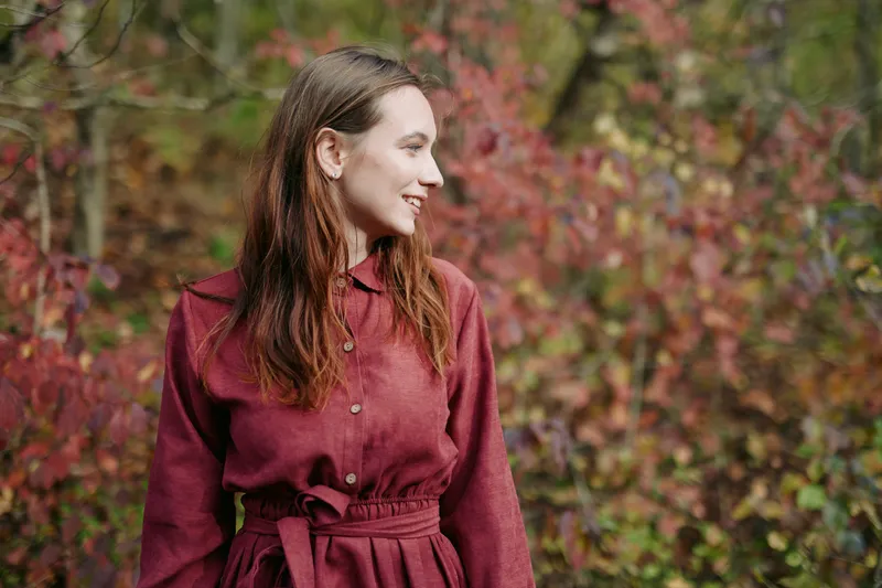 An authentic portrait of a woman in a burgundy dress amid autumn foliage, capturing genuine warmth, natural light, and real presence that conveys trust and sincerity.