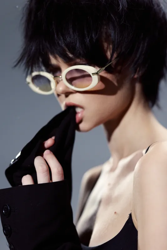 Stylish woman with short hair wearing white sunglasses biting black fabric, fashion concept with edgy and modern look.