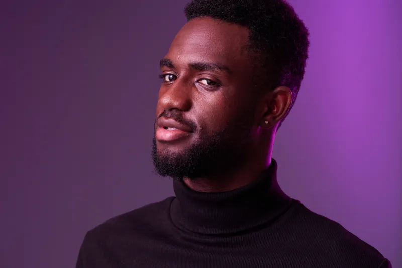 Confident young African man in a stylish black turtleneck against a purple gradient background, exuding charisma and modern fashion