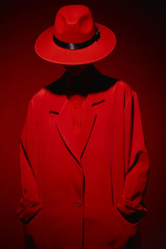 Mysterious person dressed in vivid red coat and hat, partially hidden face under shadow. Studio shot with saturated lighting. Creative concept for fashion and beauty art.