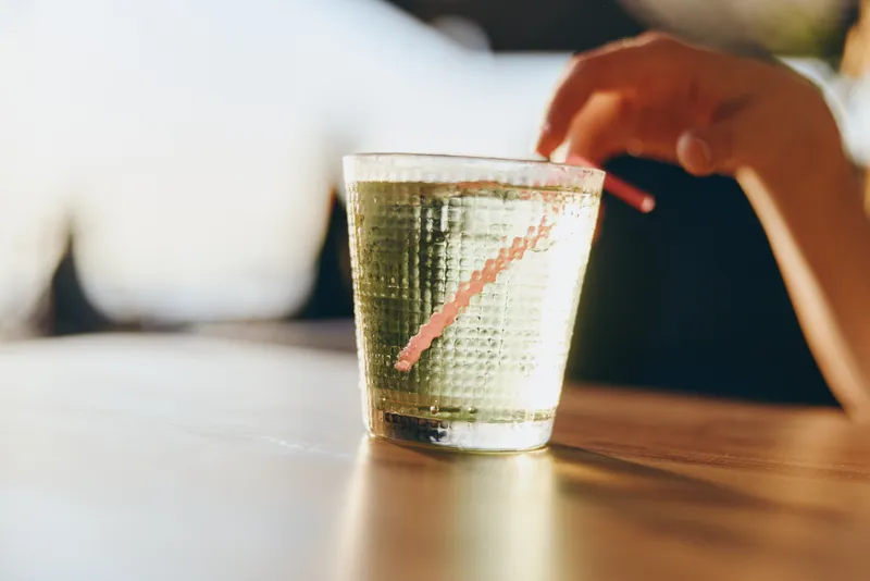 Clear glass of fresh water on wooden table with hand reaching, warm natural light, calm atmosphere, refreshing beverage, minimalistic style with soft background.