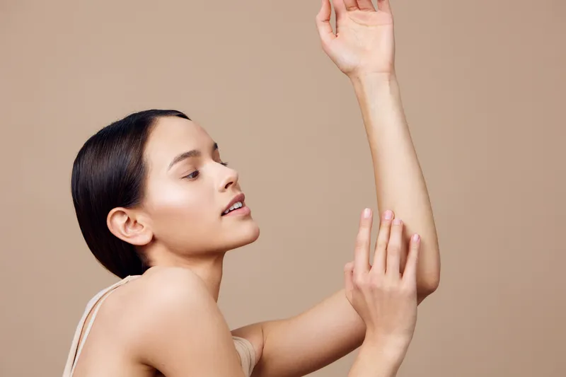 Young woman with smooth skin poses gracefully on a beige background, showcasing beauty and elegance, highlighting skincare and wellness concepts in a minimalistic style