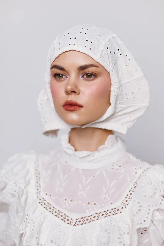 Elegant portrait of a young woman showcasing traditional style with a white embroidered bonnet and dress, conveying serenity and nostalgia