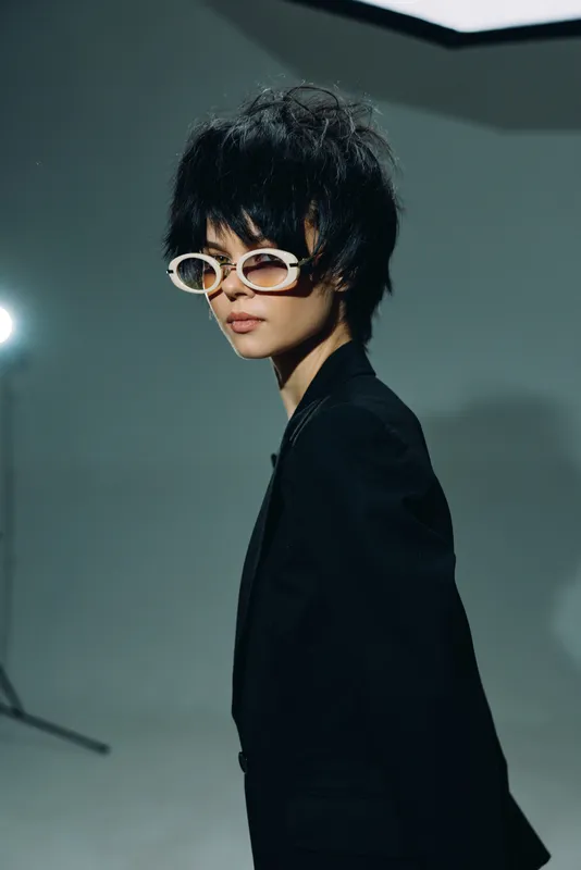 Stylish Asian woman wearing sunglasses and black jacket in moody studio lighting with dark background