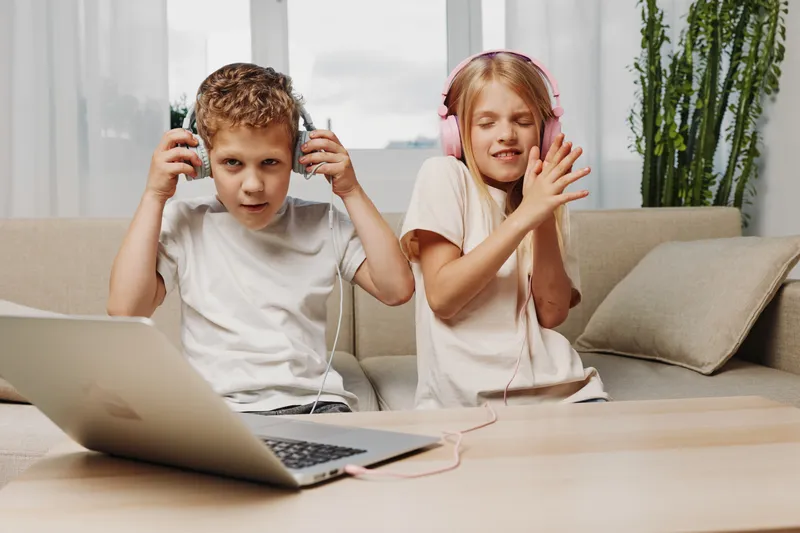 Two children listen to music with headphones, enjoying their time in a cozy living room with natural light and relaxed atmosphere. Concept of childhood and leisure.