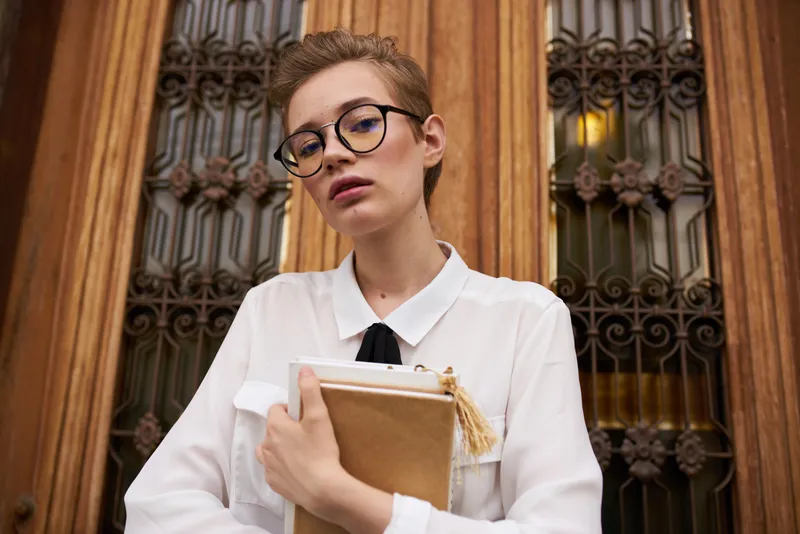 Студентка в очках с книгой в руках у высокой двери здания учебного института