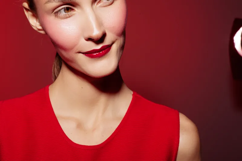 Close-up of a smiling woman in a red dress with red lipstick against a red background. Concept of fashion, beauty, and confident female portrait in studio lighting.
