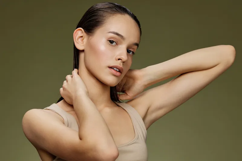 Portrait of a young woman with medium skin tone, showcasing a natural beauty look against a muted green background, emphasizing skincare and self care