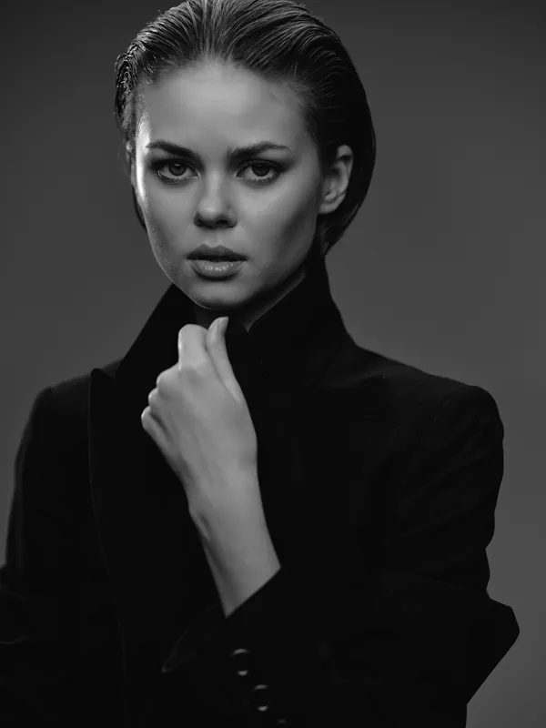 Black and white portrait of serious woman with slicked hair wearing dark clothing in studio lighting