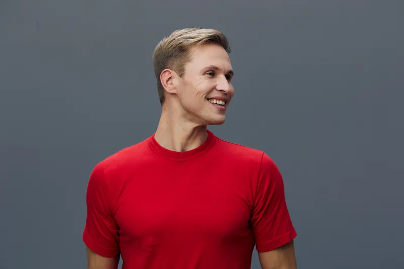 Smiling man young adult in red t-shirt pose cheerful looking away isolated on gray background studio portrait. People lifestyle concept