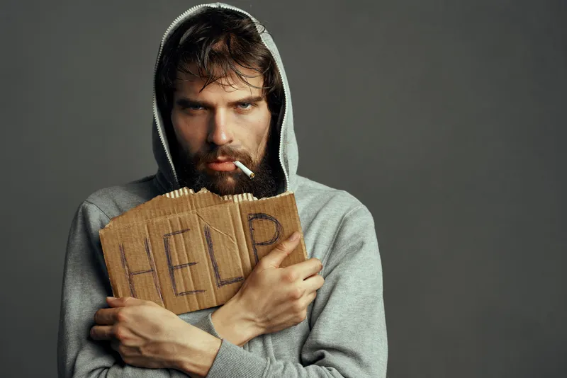 Бородатый мужчина с табличкой «Help» и сигаретой просит деньги