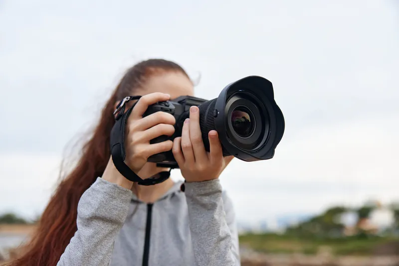 Young woman photographing nature with a DSLR camera, showcasing passion for photography against a natural outdoor backdrop