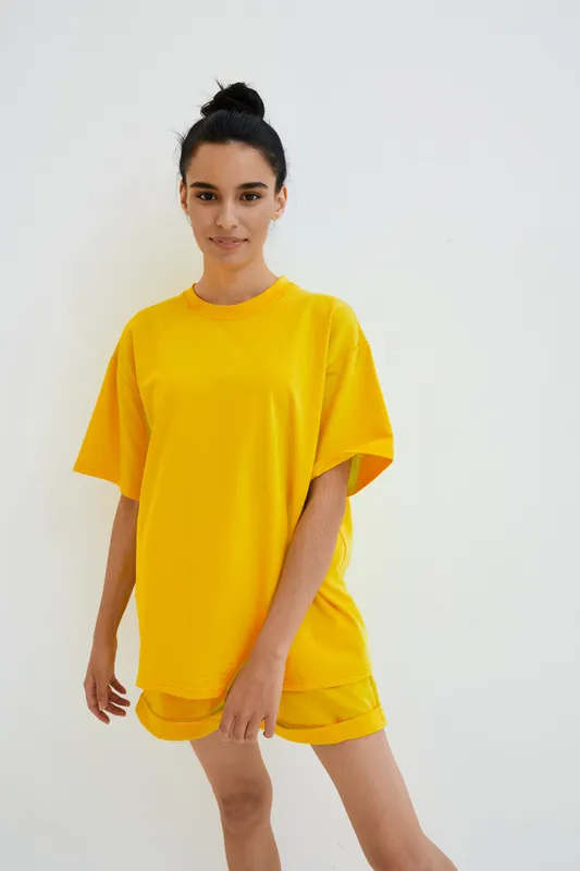Young woman in bright yellow casual outfit poses confidently against white background, showcasing modern minimalism and vibrant summer fashion style.