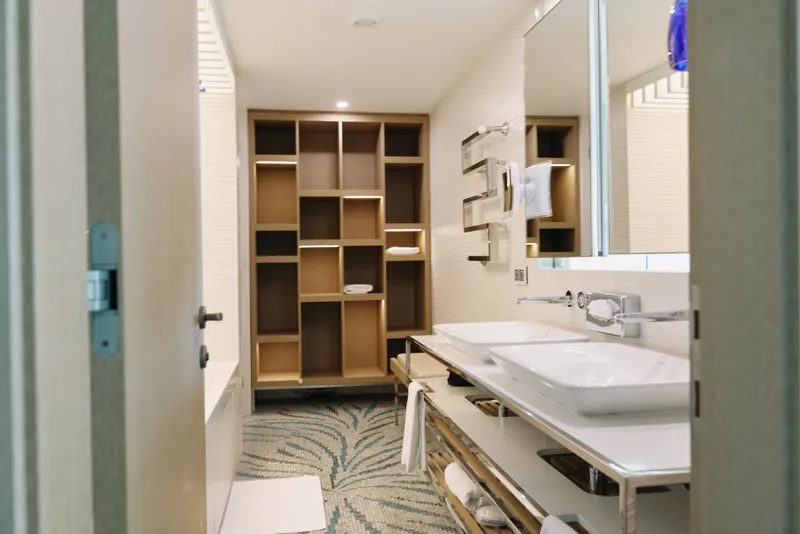 Modern bathroom interior with double sinks, wide vanity and open shelves for towels and accessories; a clean, organized space with soft lighting and a large mirror.