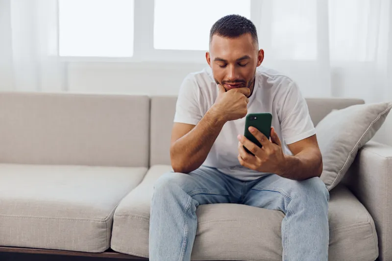 Thoughtful man browsing his phone, reflecting on digital connections and personal growth in the realm of mental health, anxiety, and modern living.