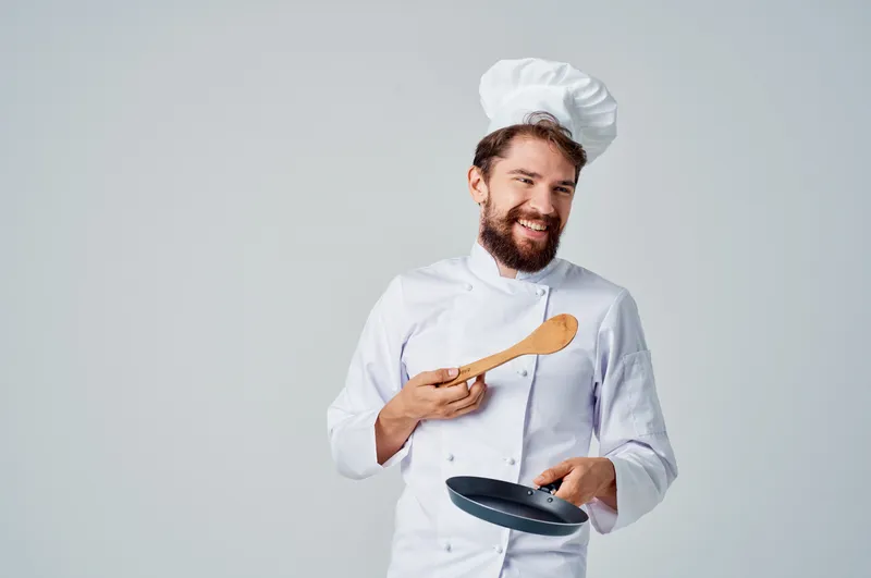 Повар с кухонной утварью работает на кухне ресторана