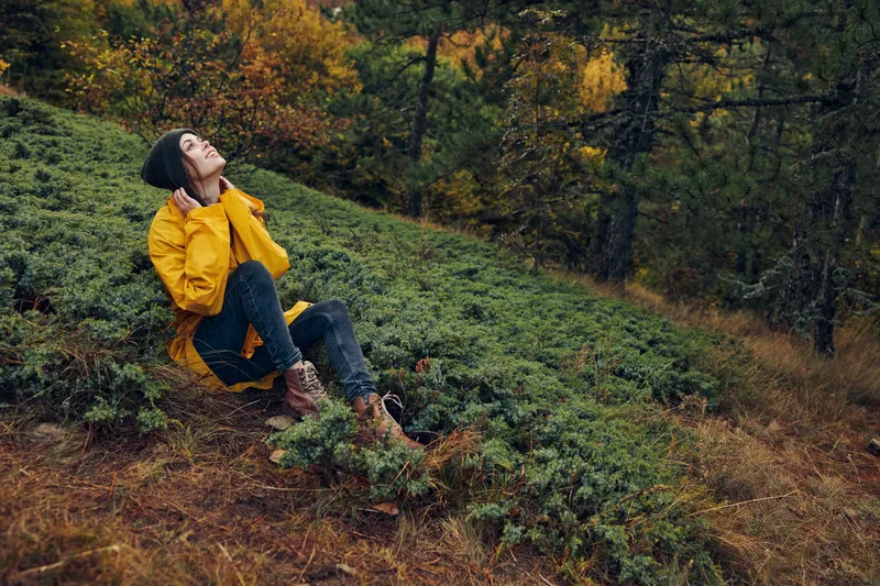 Мгновение уединения и покоя: женщина в жёлтом дождевике сидит на холме посреди безмятежного леса