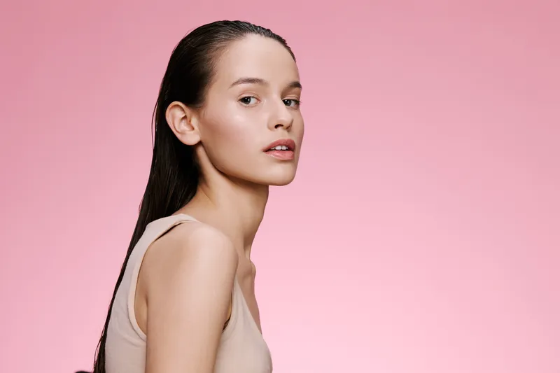 Elegant model with glowing skin, posing against a soft pink background, showcasing natural beauty and minimalistic style, ideal for skincare and beauty campaigns