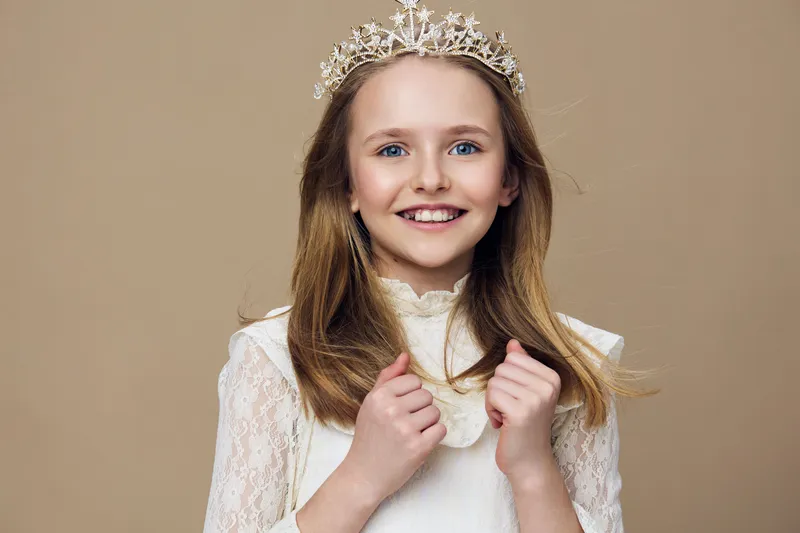 Happy young girl with a charming smile wearing a royal crown on a neutral background, representing beauty, innocence, and childhood joy
