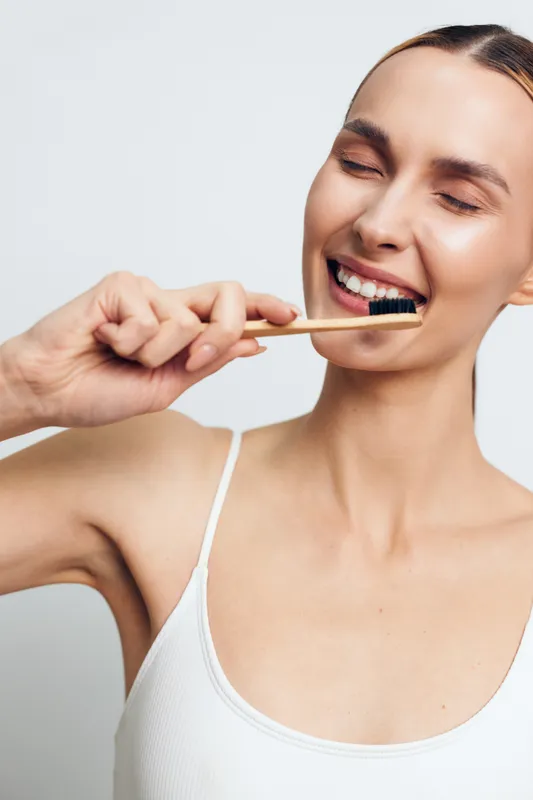 Woman with toothbrush brushing teeth, bright smile and clean oral hygiene in studio closeup, white background, healthy dental care, fresh breath mood, vertical crop