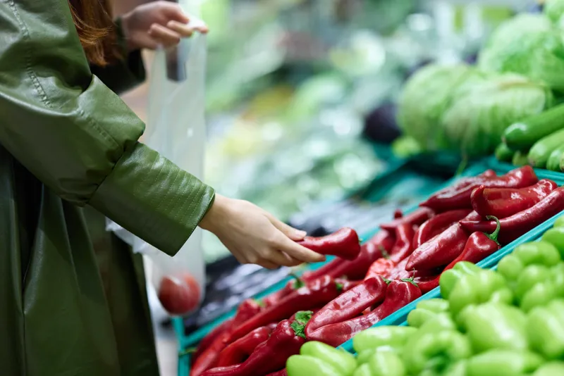 Женщина в продуктовом магазине выбирает свежие овощи для приготовления ужина, совершает покупки