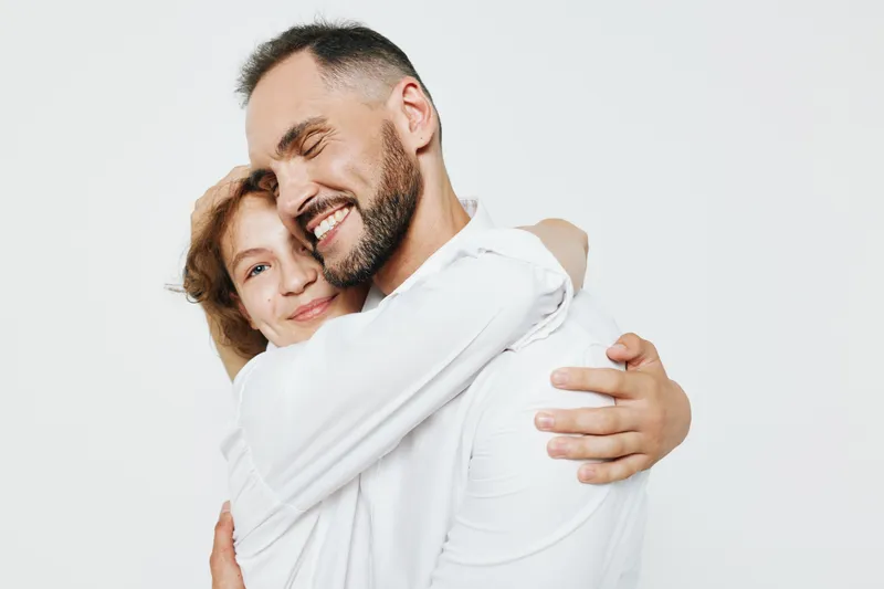 A professional man in business attire shows a warm emotion as he embraces a colleague, standing on an isolated white background, radiating confidence and teamwork.