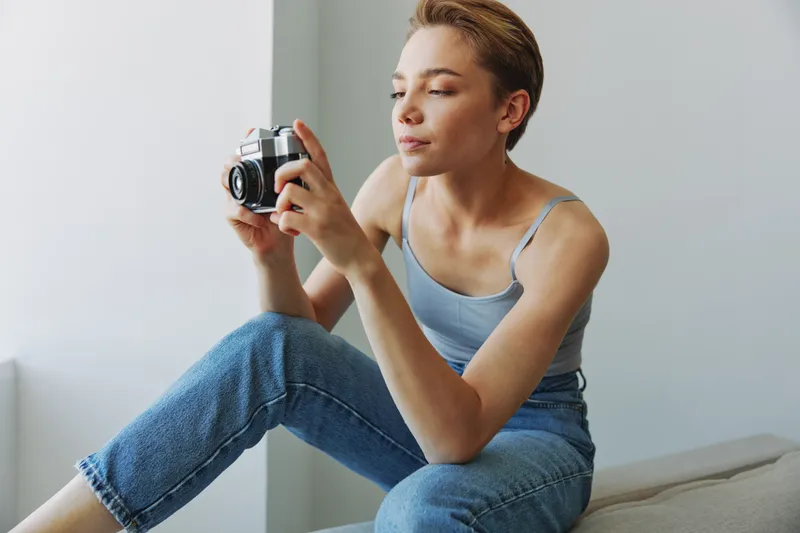 Женщина-фотограф снимает в студии на старую плёночную камеру, сидя дома на диване