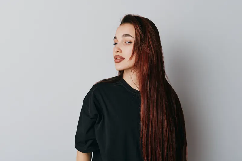 Young woman with long red hair wearing black shirt posing with confident expression on white background. Beauty, fashion, hairstyle and casual style in studio portrait photography.