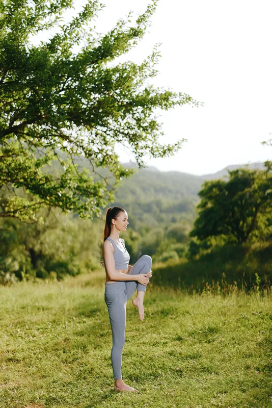 Female model practicing yoga in a serene green landscape, showcasing flexibility and tranquility in a summer setting