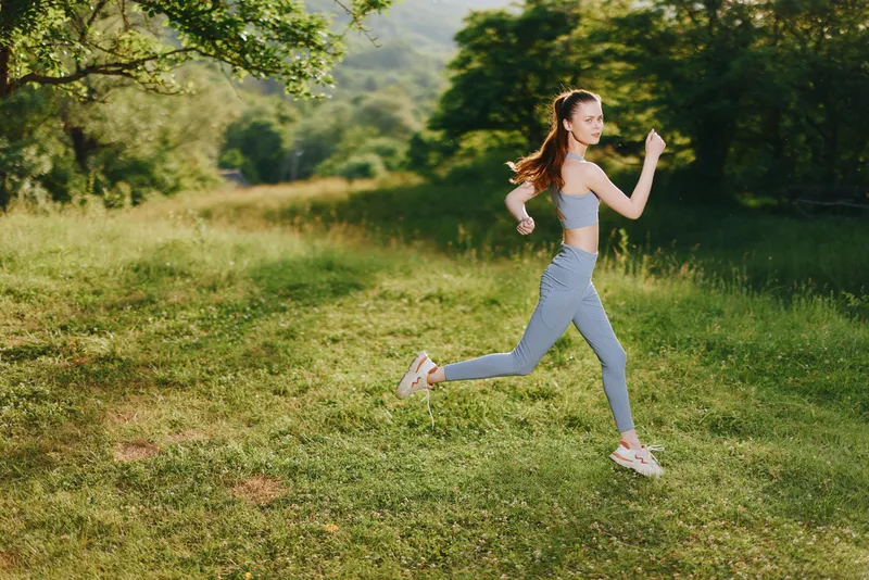 Young athletic woman running in nature, wearing blue activewear, showcasing fitness and vitality in a vibrant green meadow, representing health and exercise