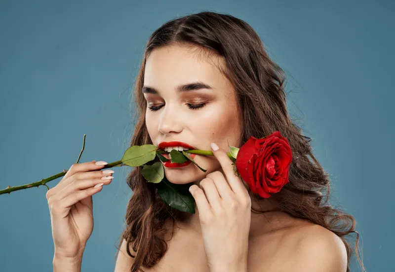 Женщина с розой в зубах, вечерний макияж, синий фон, модель