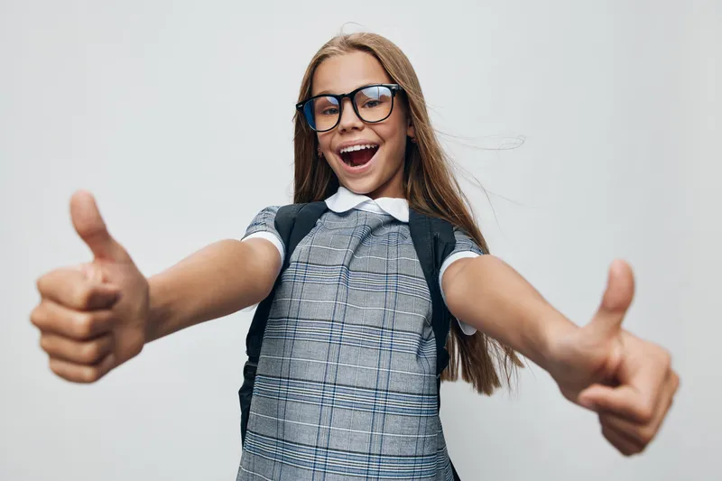 Smiling girl with glasses showing thumbs up gesture for approval, happiness and confidence with casual outfit on white background. Positive, cheerful and young teenager.
