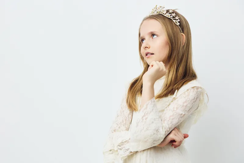 Elegant girl in a white dress contemplating with a thoughtful expression, showcasing innocence and grace against a minimalistic background