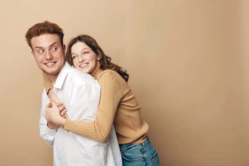 Happy young couple in casual clothes smiling and hugging each other on beige background. Concept of love, friendship, relationship, and positive emotions.