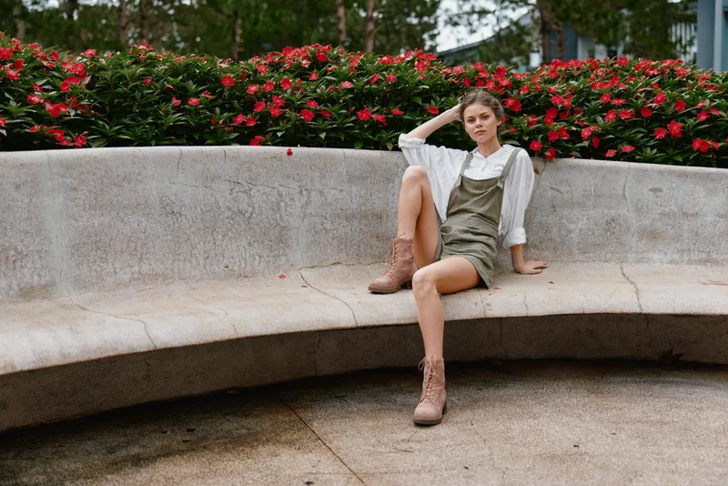 Stylish young woman in a casual outfit enjoying a sunny day in a park, surrounded by blooming flowers, embodying a relaxed and carefree summer vibe