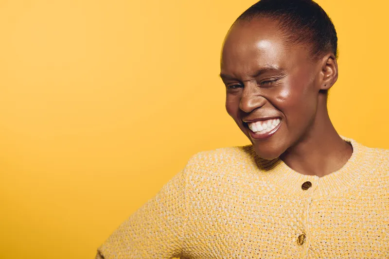 Happy smiling dark skinned African woman in yellow sweater winks with eyes closed on yellow background. Concept of positive emotions, joy, and confident black female model portrait.