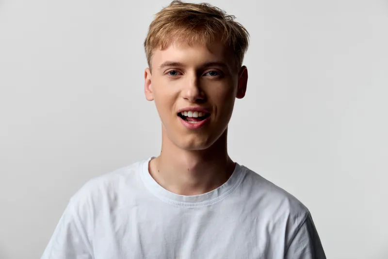 Smiling young man in a white tee with a friendly, relaxed expression for lifestyle stock, studio lighting, clean background, and casual look.