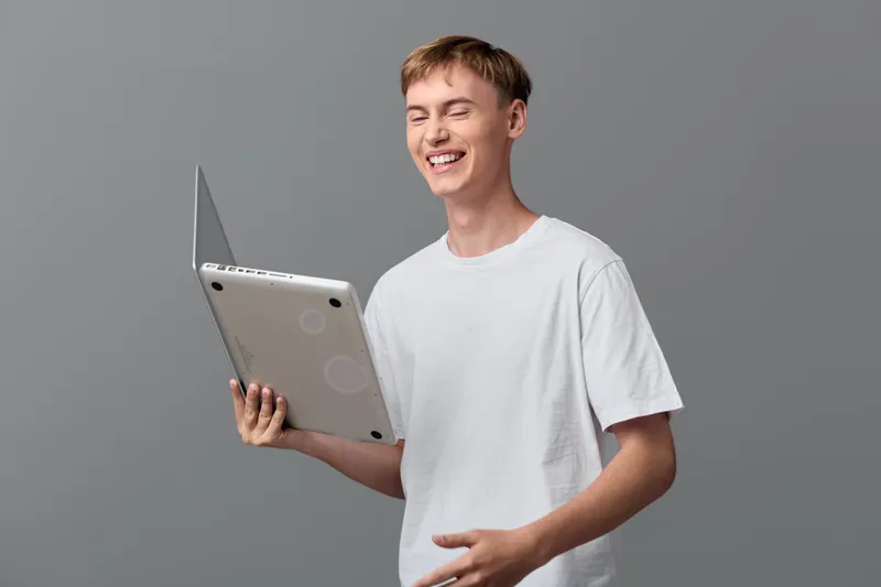 Young man holding a tablet and laptop, smiling in a casual shirt, showcasing everyday digital work and learning, bright and approachable mood, modern tech lifestyle and productivity